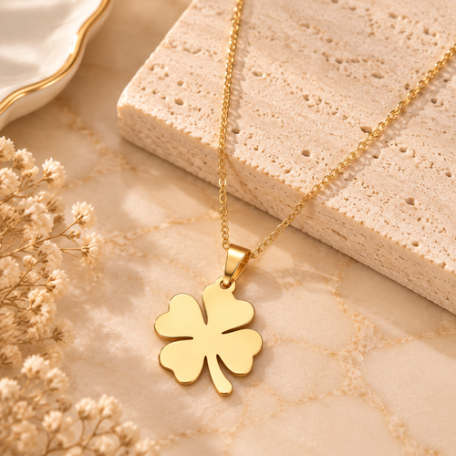Gold tone four leaf clover pendant necklace displayed on soft beige marble background
