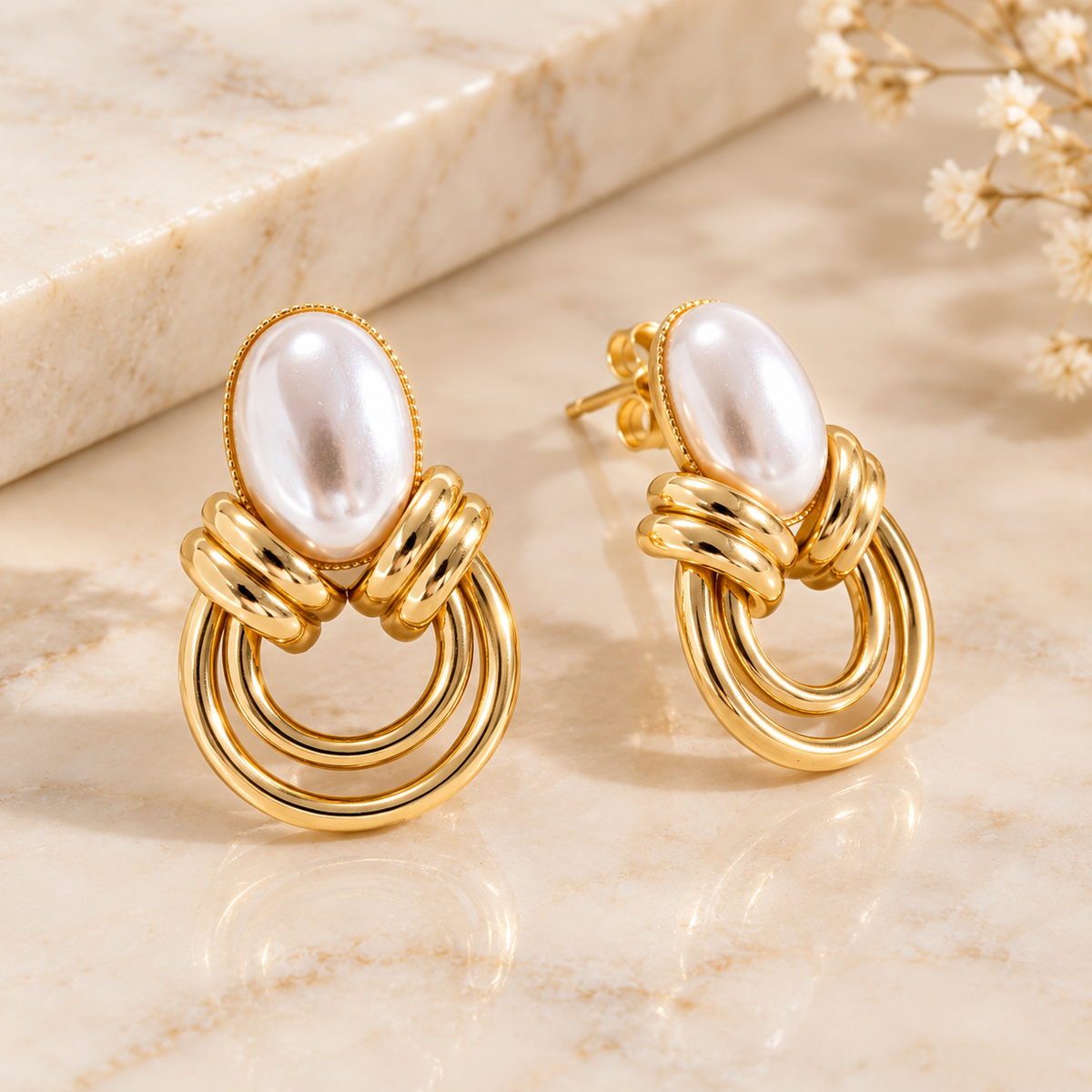 Gold-tone pearl drop earrings shown from an angled view on a marble surface