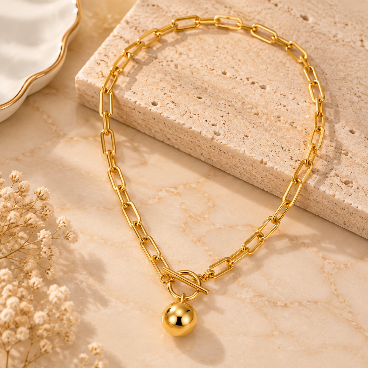 Minimalist gold tone paperclip chain necklace with sphere pendant displayed on beige marble background