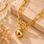 Close up detail of gold tone stainless steel necklace with toggle clasp and sphere ball pendant